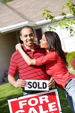 african american couple holding a sold sign next to their house